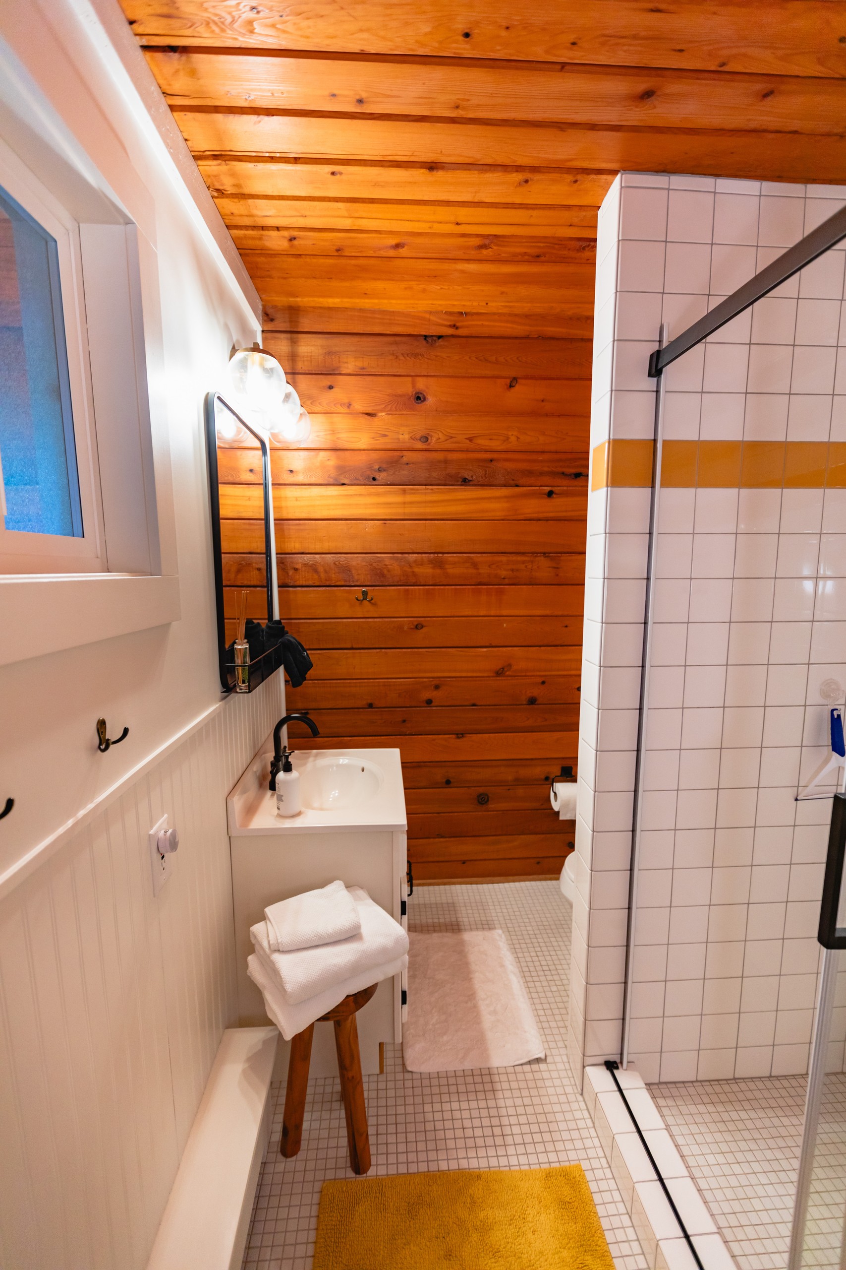 Bathroom with a white vanity, wood-paneled walls and a white tile shower with a yellow stripe