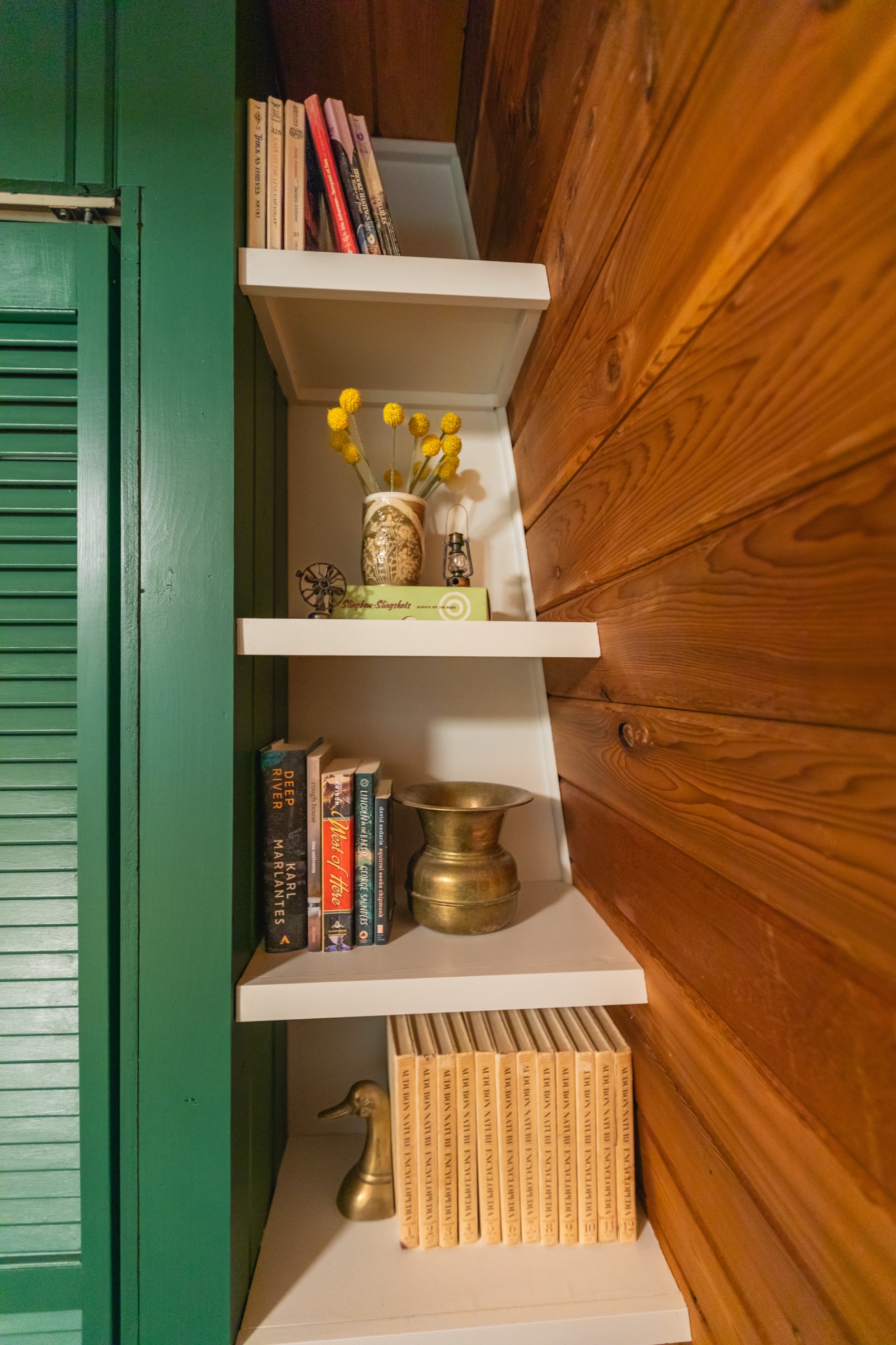 Corner shelving with vintage books, a brass duck and yellow dried flowers