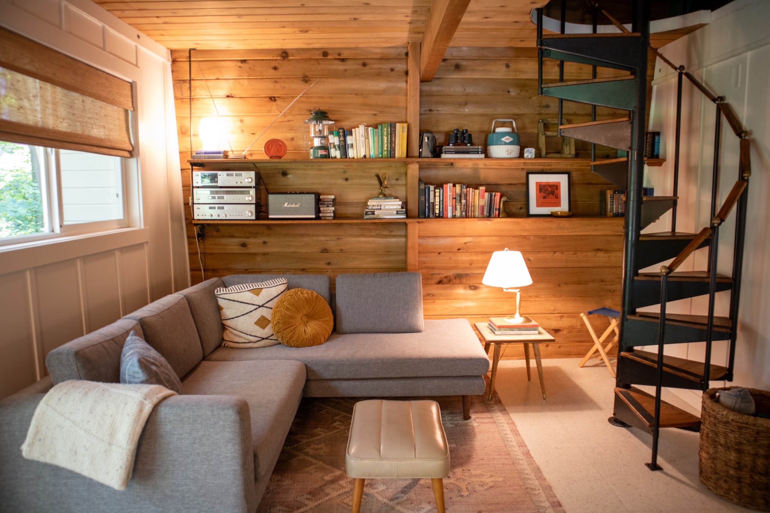 Downstairs living room with wood paneling, grey sectional, vintage books and a black spiral staircase