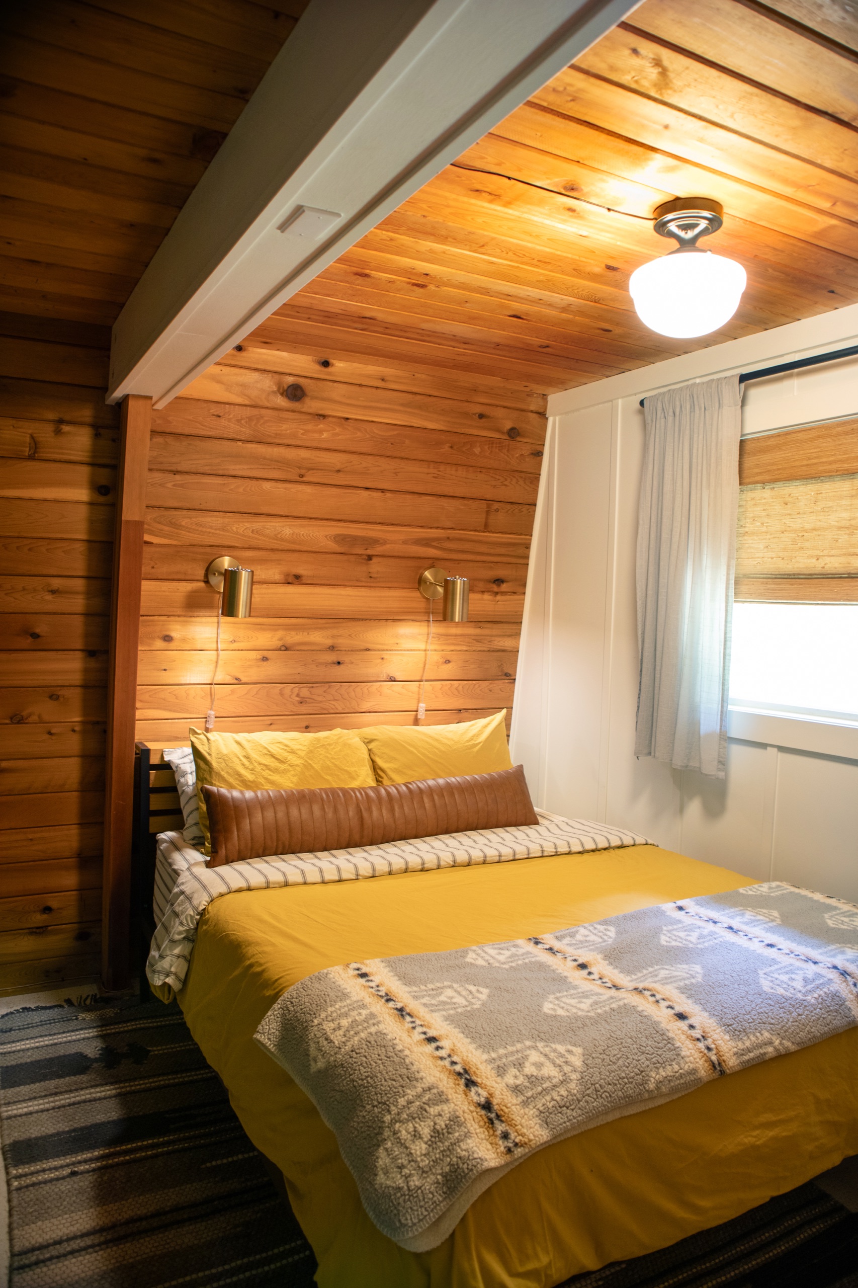 Primary bedroom with wood-paneled walls, brass sconces and mustard yellow bedding