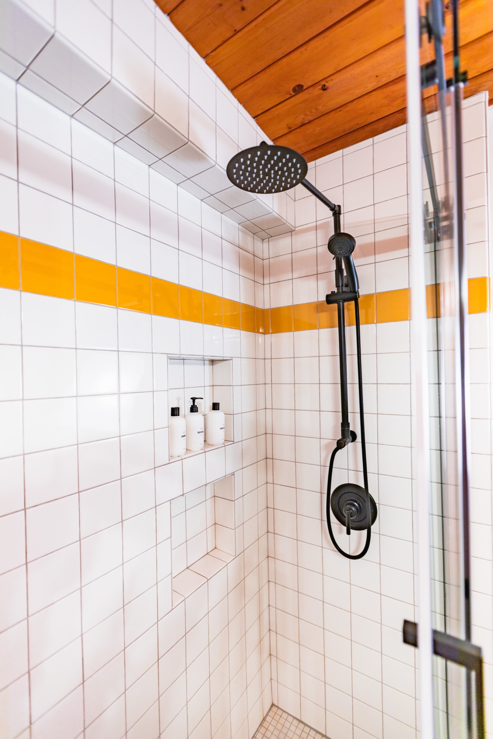 After: white subway tile shower with a yellow tile stripe and black rain shower head