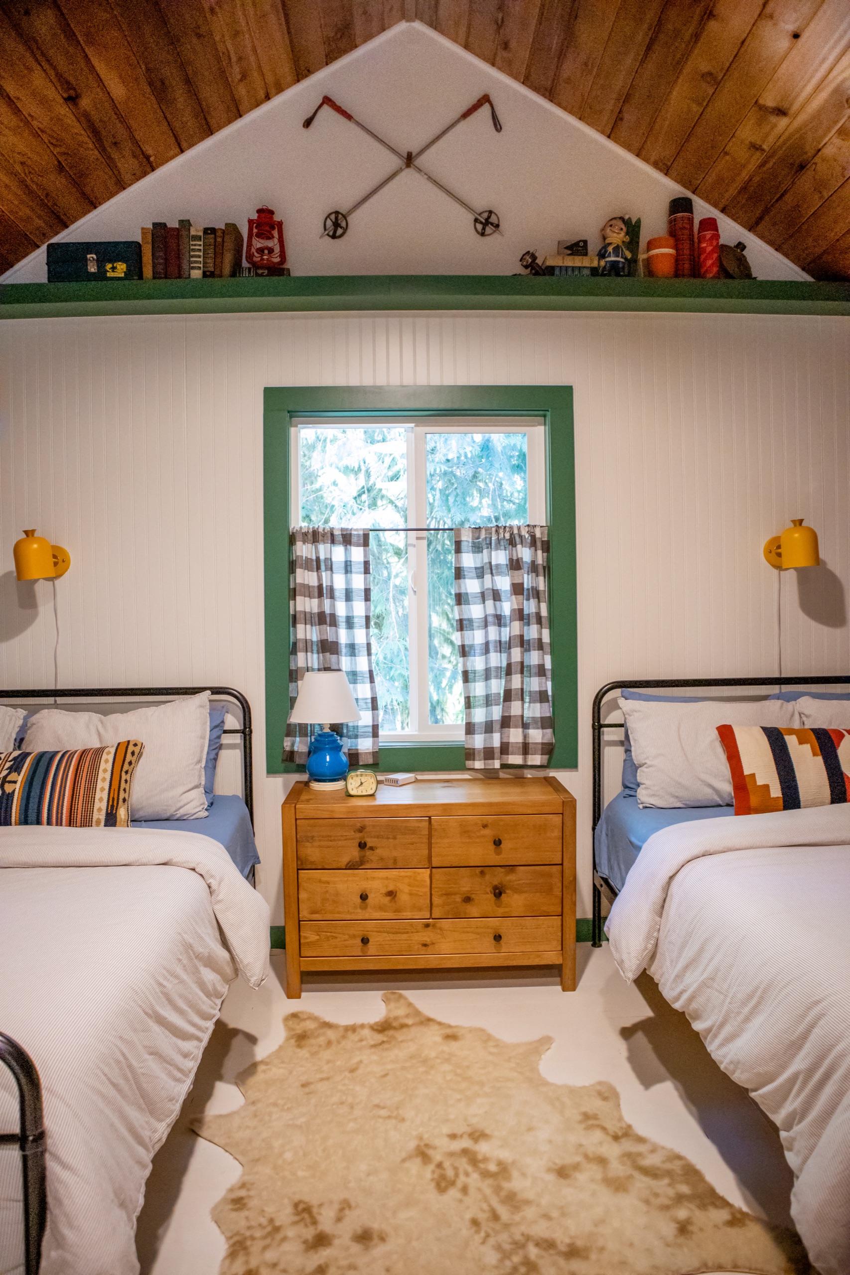 After: two queen beds with plaid curtains, yellow sconces and a cowhide rug